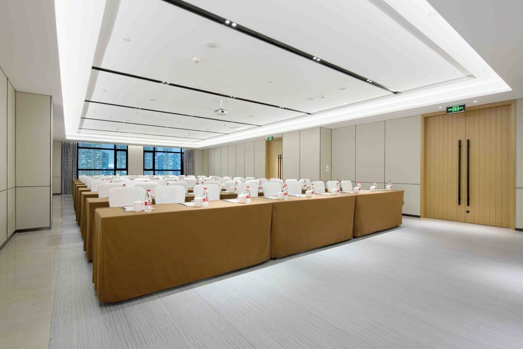 Un salón de conferencias con mesas largas, sillas blancas y un techo alto con iluminación empotrada.