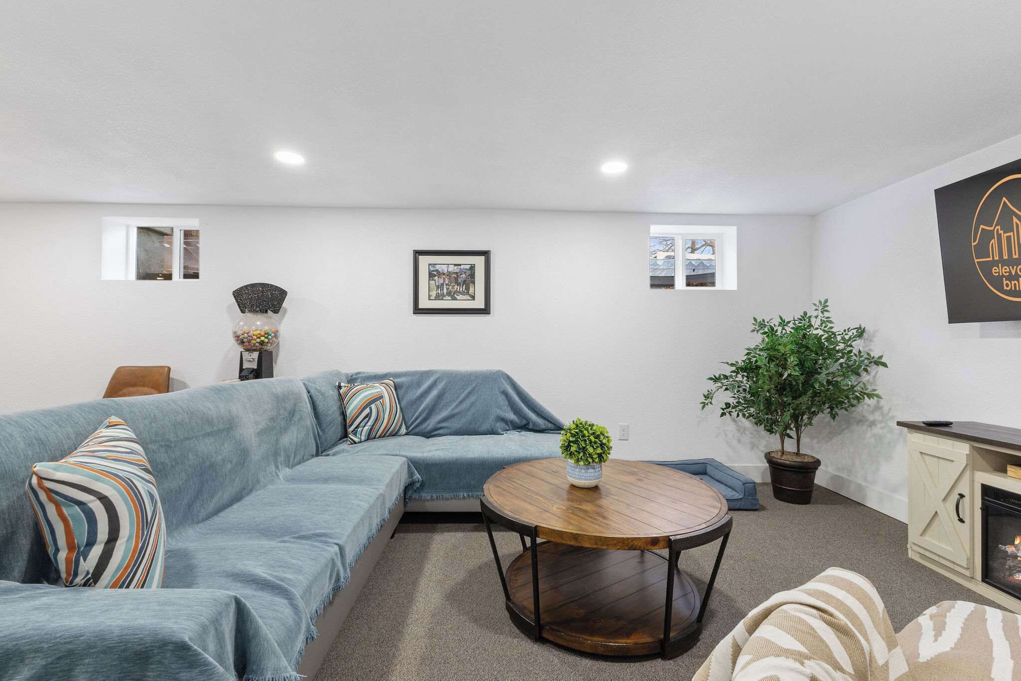 A modern living room with a sectional sofa, a round wooden coffee table, a potted plant, and a fireplace.