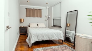 A bedroom with a bed, bedside tables, a mirror, and a window with curtains. - Charming Two-Bedroom NYC Escape Backyard (New York)