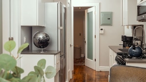 A modern kitchen with white cabinetry, a stainless steel refrigerator, a globe decoration, and a blue kettle on the stove. - Charming Two-Bedroom NYC Escape Backyard (New York)