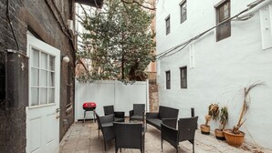 A courtyard with wicker furniture, a barbecue grill, and potted plants. - Charming Two-Bedroom NYC Escape Backyard (New York)