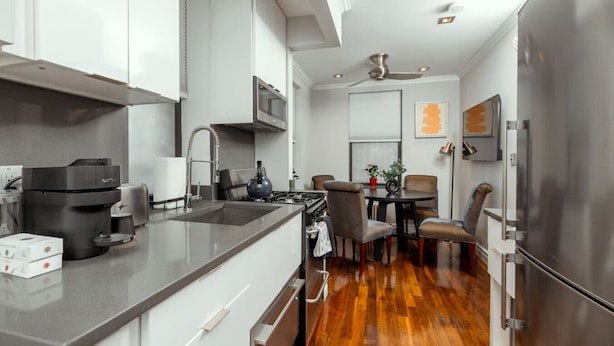 A modern kitchen with a central island, stainless steel appliances, and a dining area with chairs and a table. - Charming Two-Bedroom NYC Escape Backyard (New York)