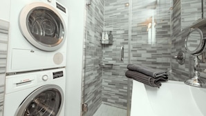A modern bathroom with a built-in washer and dryer, a glass shower enclosure, and a vanity with a mirror. - Charming Two-Bedroom NYC Escape Backyard (New York)