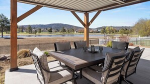 An outdoor patio with a table and chairs, a covered area, and a view of a lake and hills. - Harbor House with Hottub on 18th Hole (Klamath Falls)