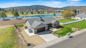 A single-story house with a garage, a small front yard, and a view of a lake and hills in the background. - Harbor House with Hottub on 18th Hole (Klamath Falls)