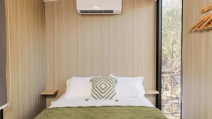 Une chambre à coucher avec un lit, une couverture verte, un oreiller à motifs géométriques, une table de chevet et une fenêtre donnant sur des arbres.
