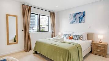 A hotel room with a bed, a nightstand, a lamp, a mirror, and a window with curtains.