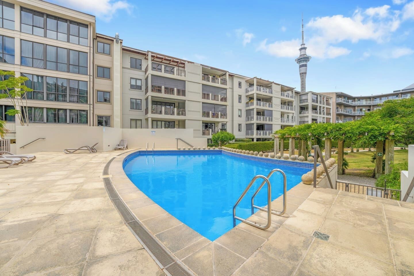A modern building with a swimming pool, balconies, and a tower in the background.