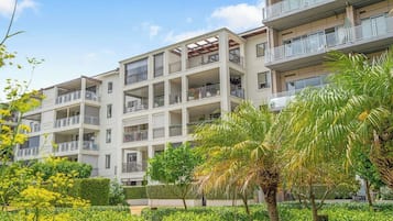 A multi-story residential building with balconies, surrounded by lush greenery and flowering plants.
