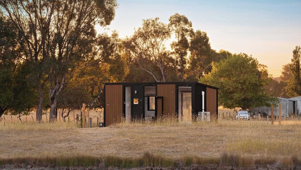 A modern, single-story building with a flat roof, surrounded by a natural landscape with trees and a body of water.