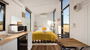 A compact, modern bedroom with a bed, bedside table, and a view of the outdoors.