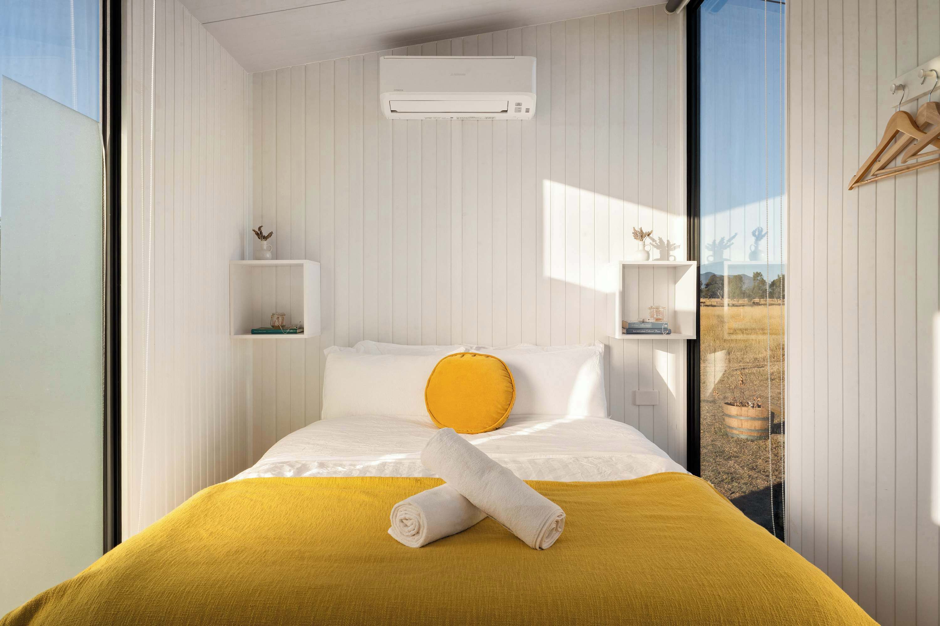 Ein Hotelzimmer mit Bett, gelber Decke, weißem Handtuch und einem Fenster mit Blick ins Freie.