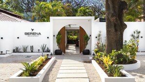 Un bâtiment blanc avec une enseigne indiquant « SERENA BEACH RETREAT » et un chemin menant à une arche.