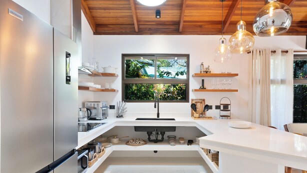 Une cuisine moderne dotée d’un réfrigérateur encastré, d’une fenêtre donnant sur un espace verdoyant et de luminaires suspendus.