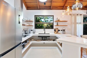 Cocina moderna con refrigerador empotrado, ventana con vista a follaje e iluminación colgante.
