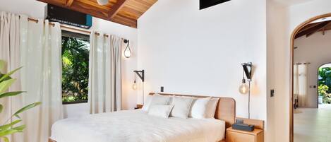 A bedroom with a wooden bed, bedside lamps, and a view of greenery outside.