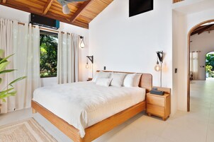 A bedroom with a wooden bed, bedside lamps, and a view of greenery outside.