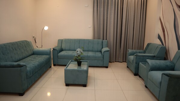 A living room with a teal sofa set, a coffee table with a plant, and a floor lamp.