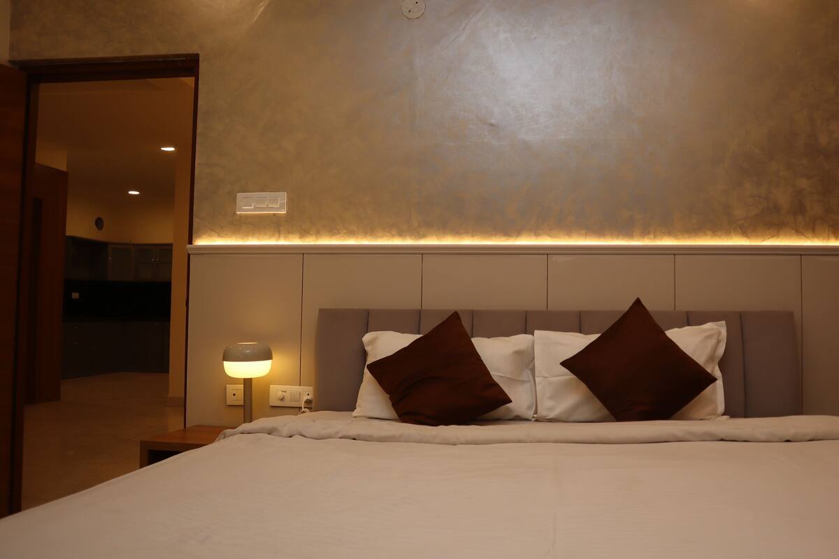 A hotel room with a bed, a nightstand, a lamp, and a wall-mounted light fixture.