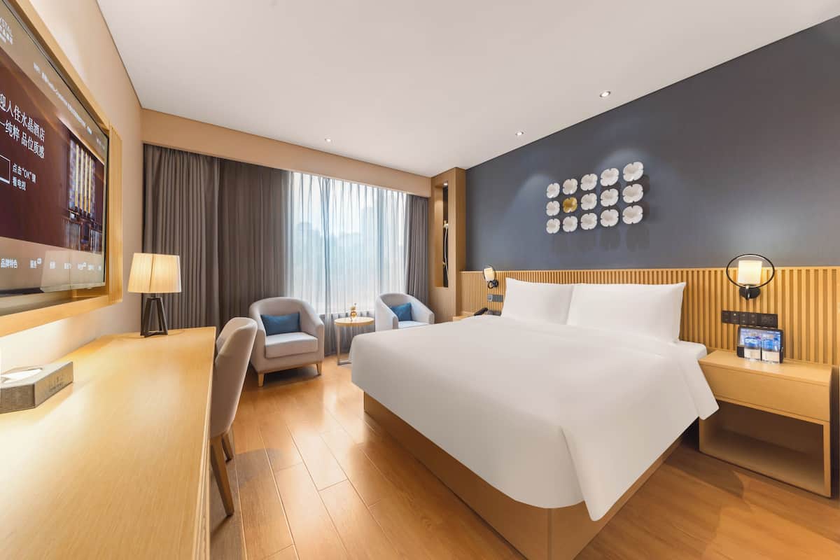 Een moderne hotelkamer met een groot bed, een bureau, twee stoelen, een televisie en een wand met decoratieve details.
