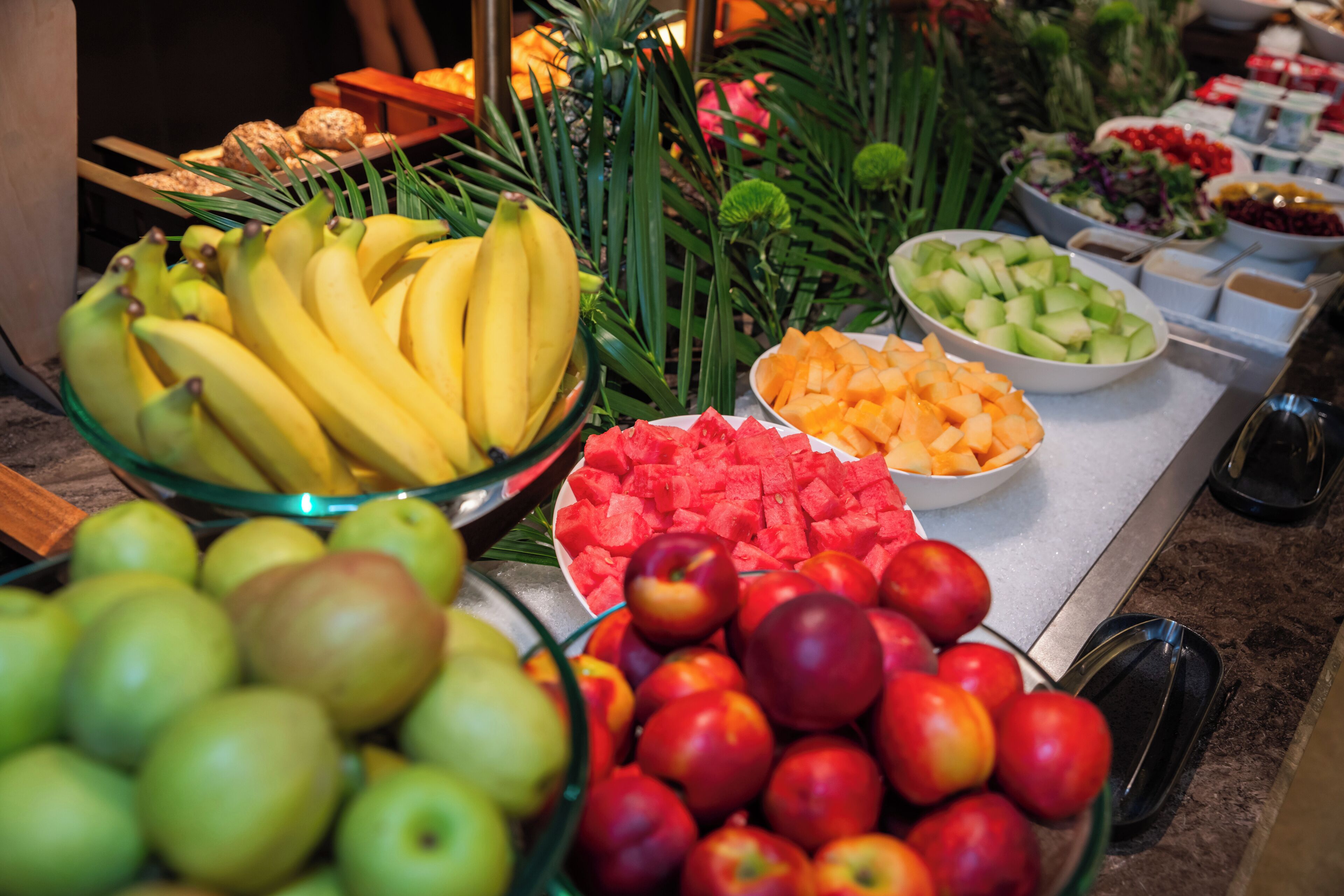 A buffet with various fruits including bananas, apples, watermelon, and melon.