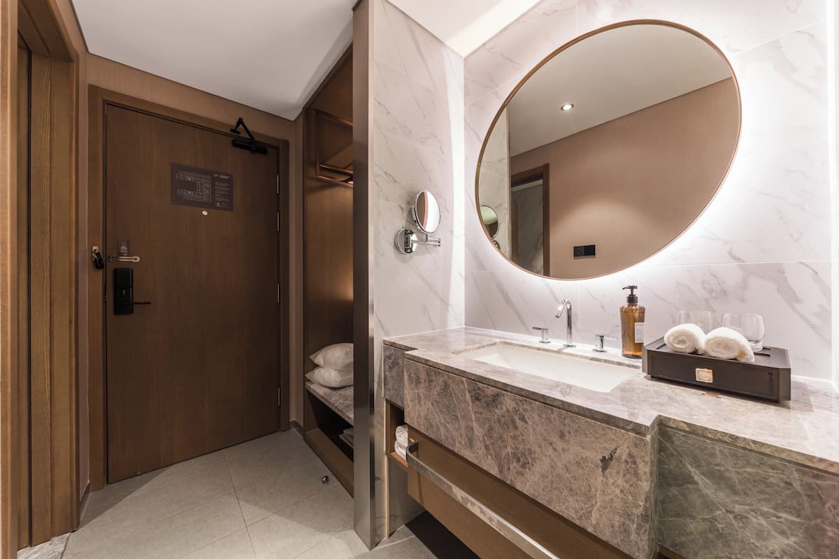 Een moderne badkamer met een marmeren wastafelmeubel, een grote spiegel, een handdoekrek en een houten deur.
