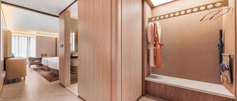 A hotel room with a wooden wardrobe, a vanity with a mirror, and a hanging coat rack.