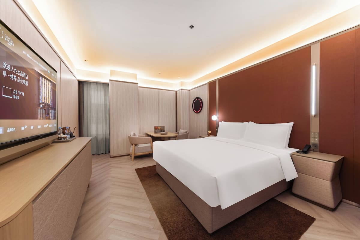 Een moderne hotelkamer met een groot bed, nachtkastje en een televisie aan de linker muur.