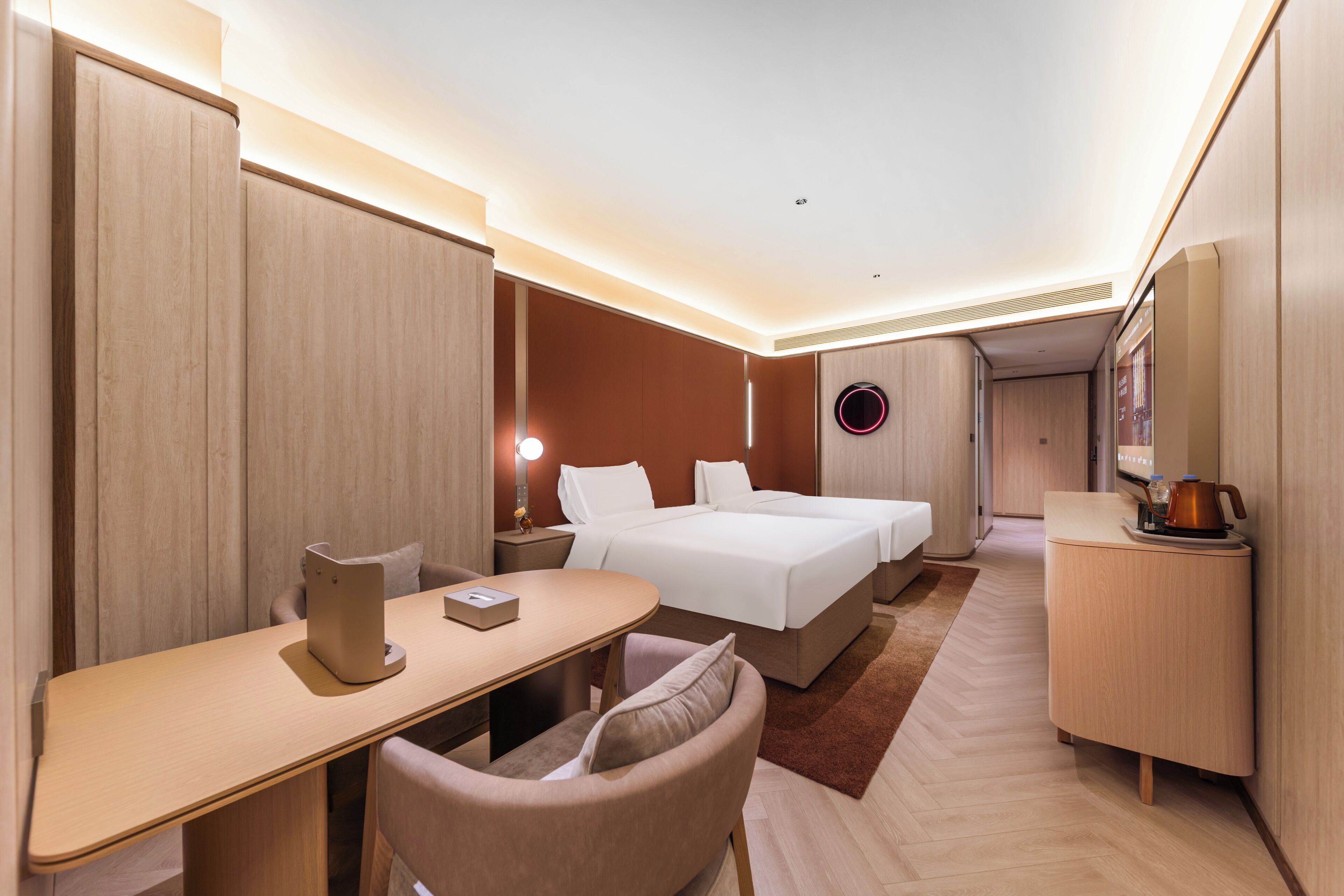 Ein modernes Hotelzimmer mit Bett, Schreibtisch, Stuhl, Nachttisch und einer kleinen Küchenzeile.