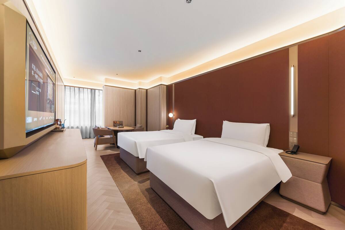 Hotelkamer met twee bedden, een bureau, een televisie en een groot raam met gordijnen.