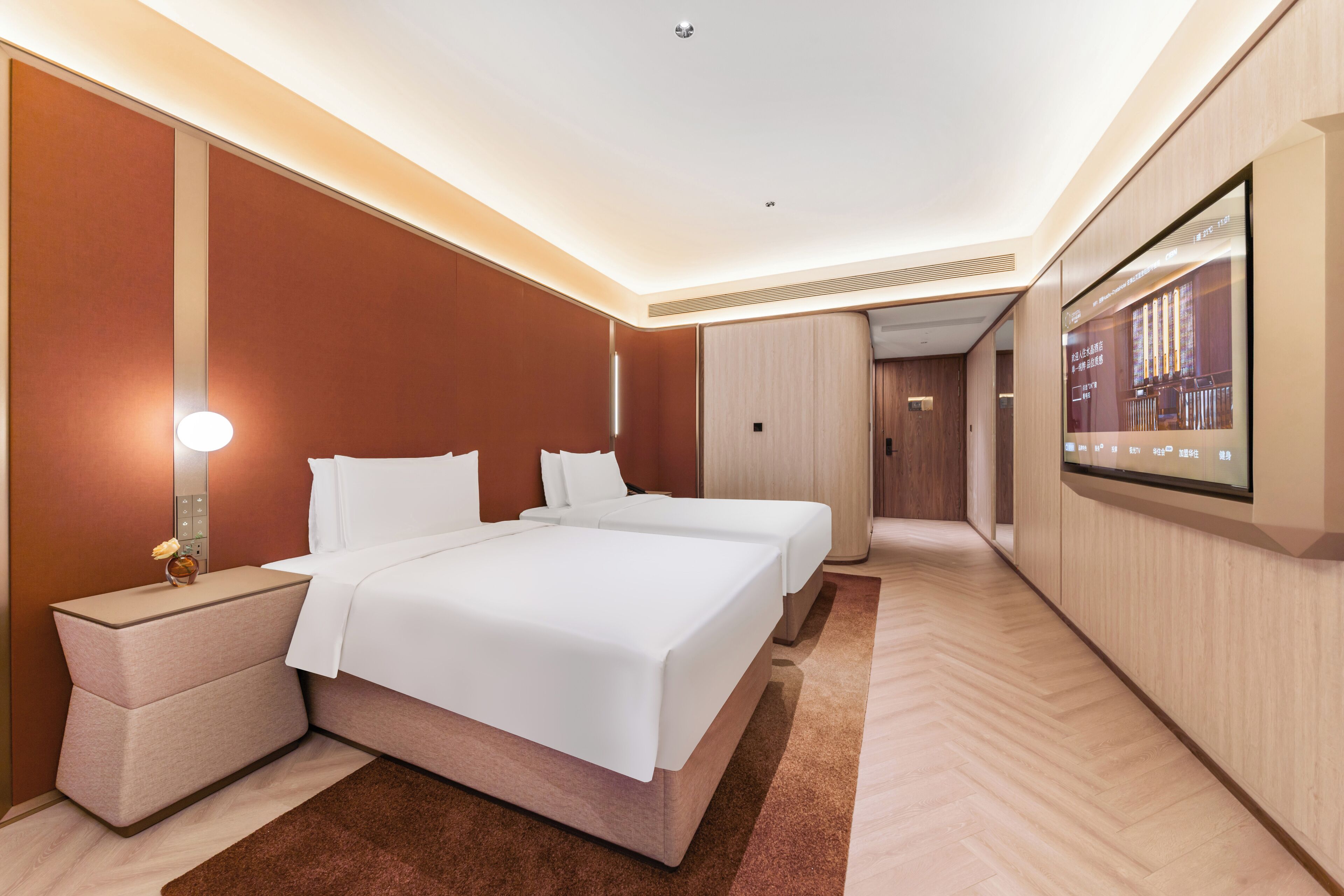 Quarto de hotel moderno com uma cama grande, mesas de cabeceira, televisão de tela plana e piso de madeira.