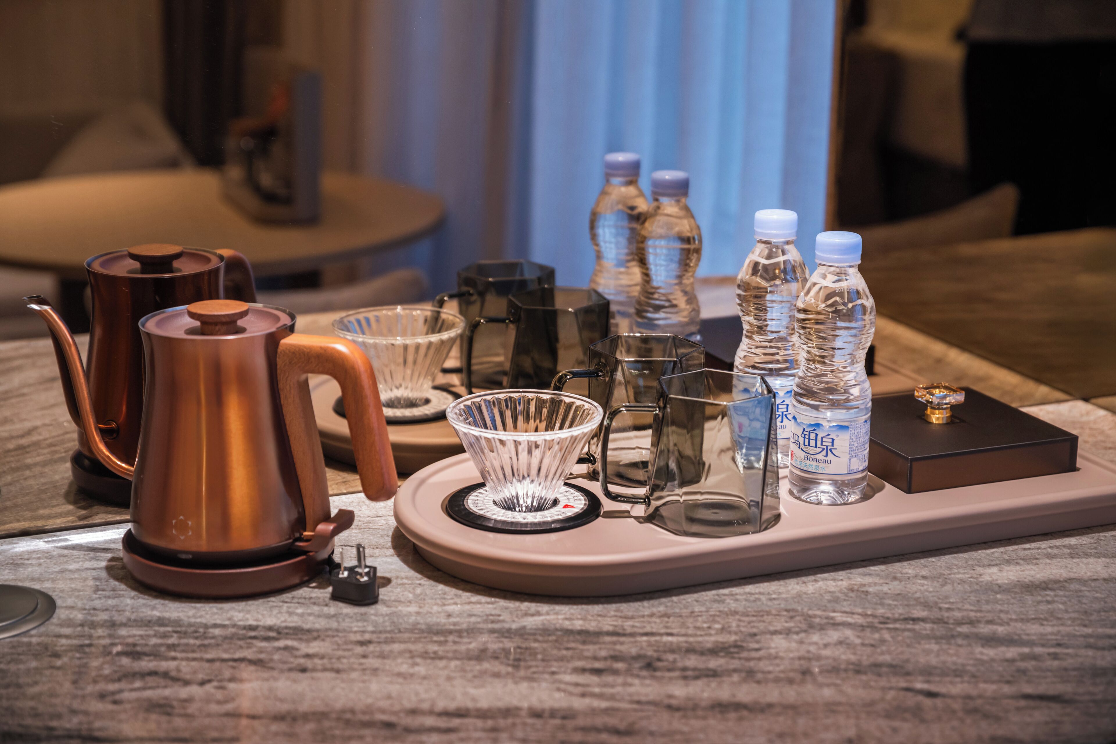 A coffee station with a coffee pot, glass cups, and water bottles on a tray.