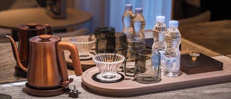 A coffee station with a coffee pot, glass cups, and water bottles on a tray.