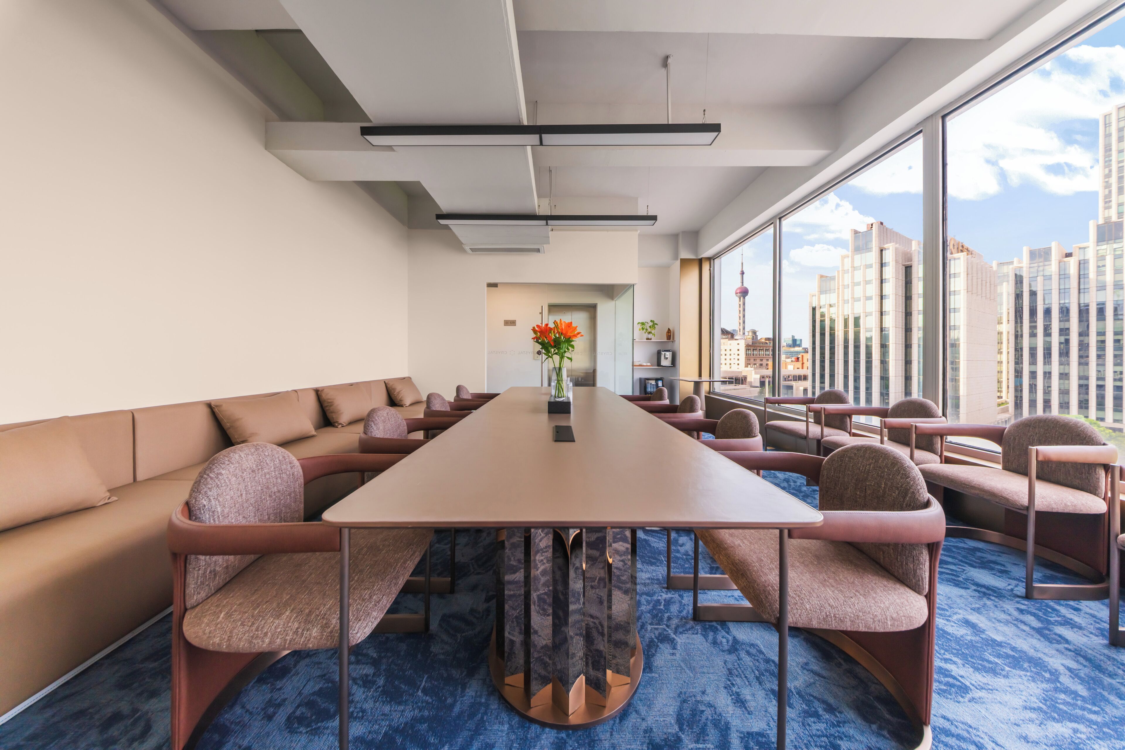 A conference room with a long table, cushioned seating, and large windows offering a city view.