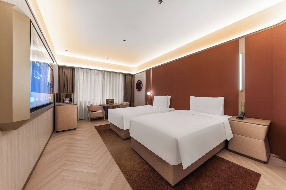 Een hotelkamer met twee bedden, een bureau, een televisie en een minibar.