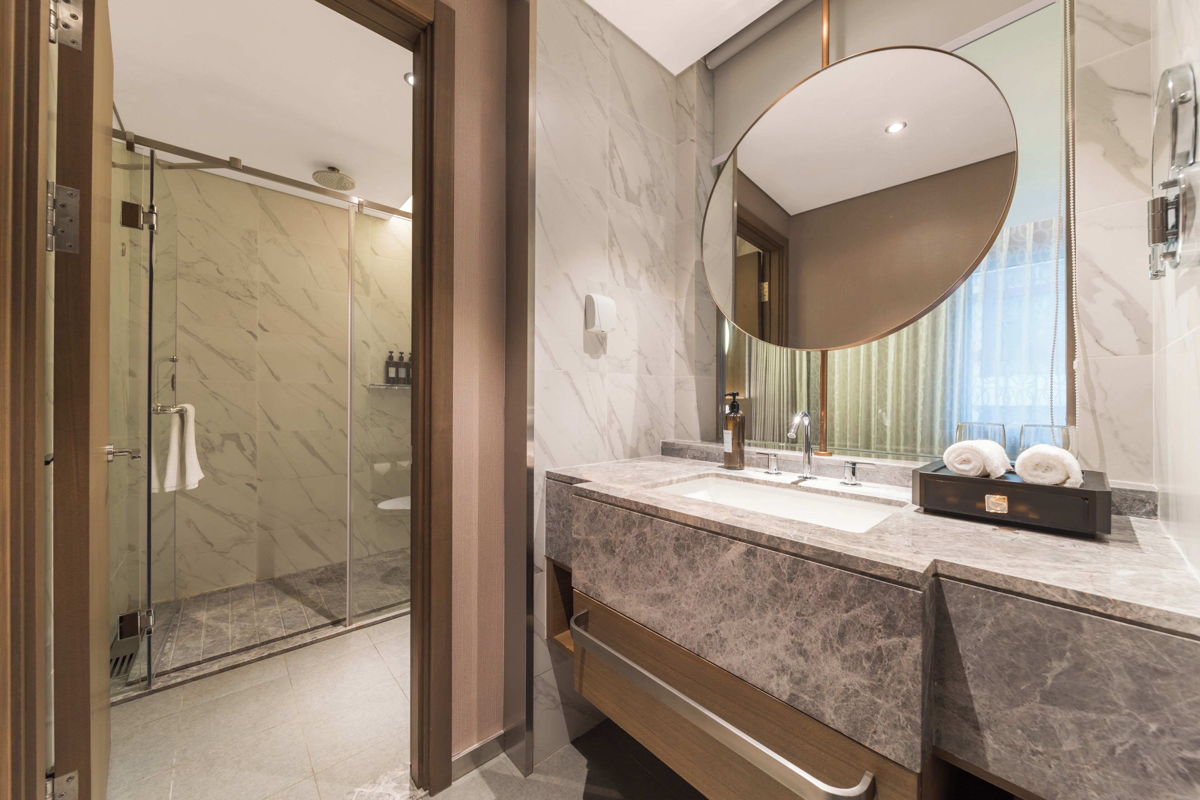 A modern bathroom with a glass shower, a marble sink, and a large mirror.