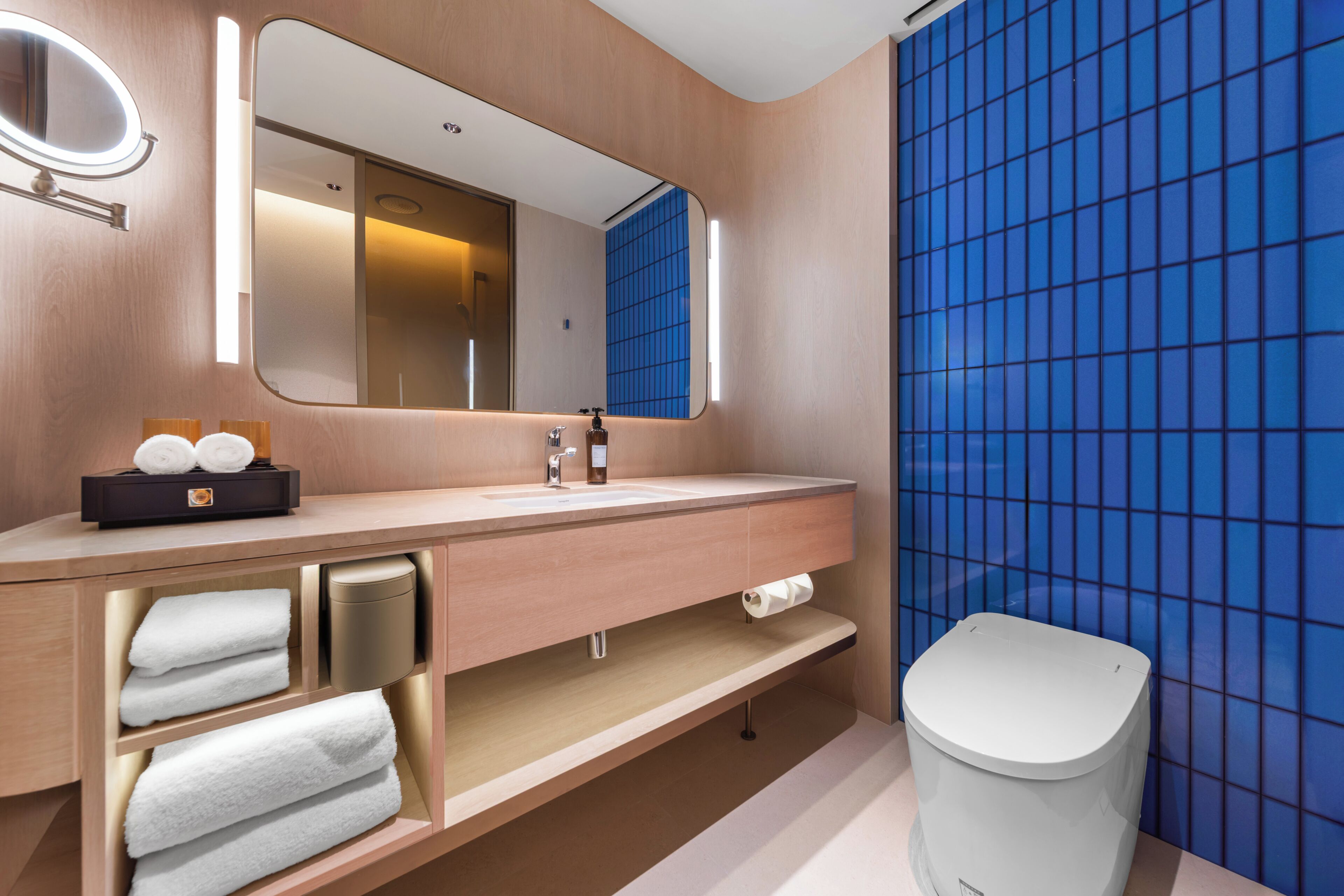 Un baño moderno con tocador de madera, un espejo grande, inodoro y paredes con azulejos azules.