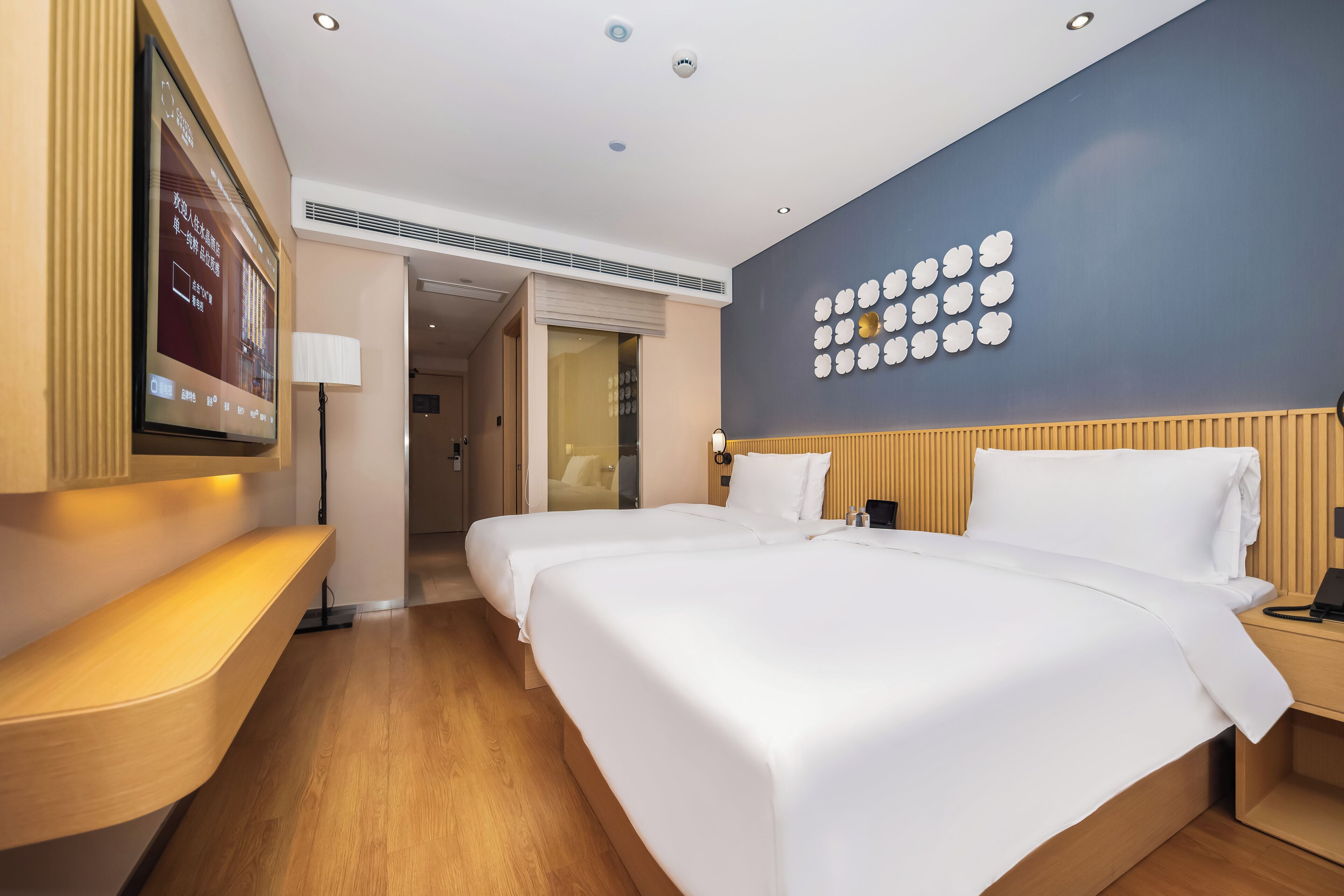 Ein Hotelzimmer mit zwei Betten, einem Fernseher an der Wand, einem Nachttisch und einer Lampe.