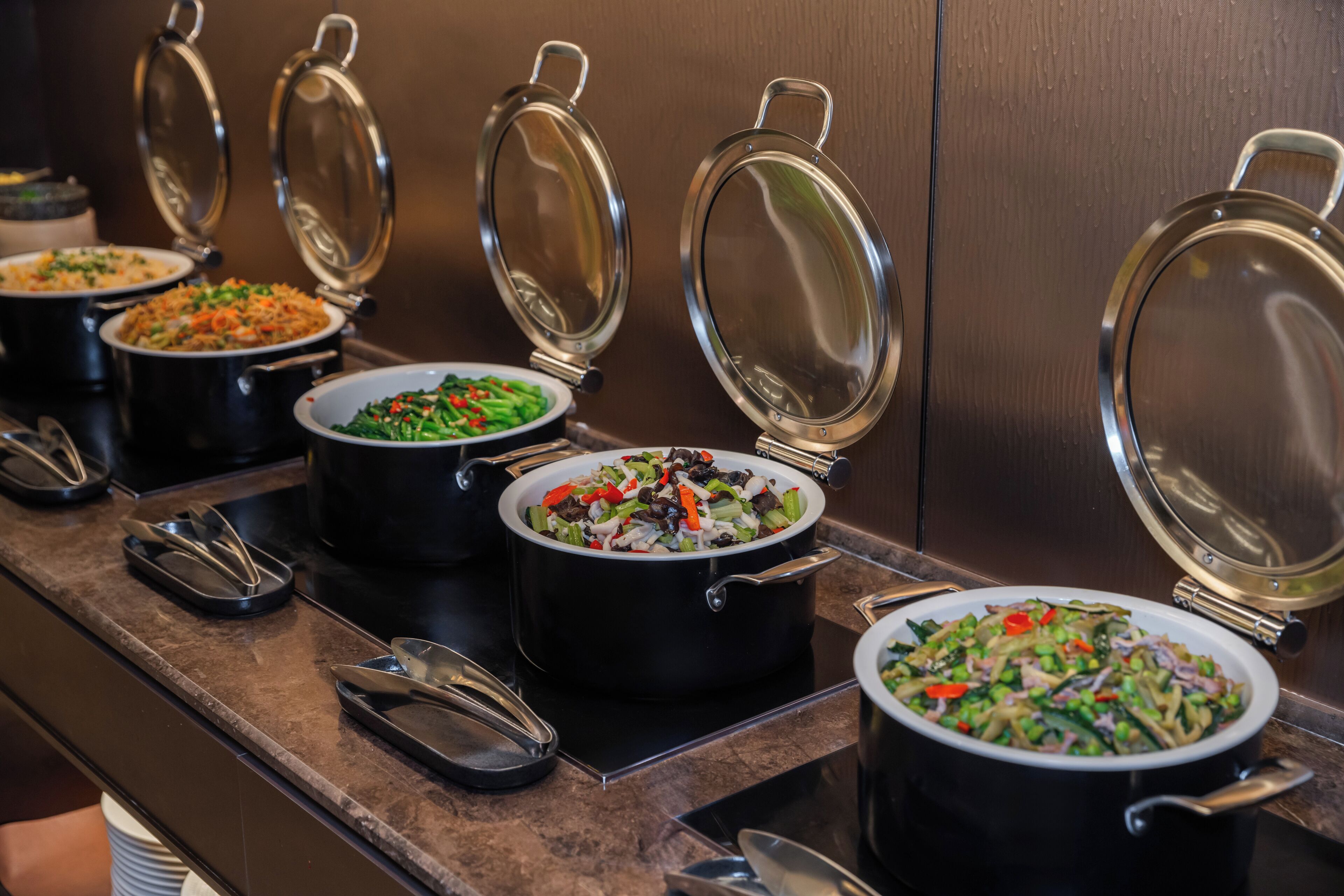 Un buffet avec plusieurs plats présentés dans des récipients noirs, chacun étant muni d’un couvercle.