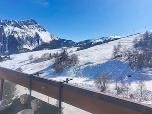 Schneebedeckte Berglandschaft mit Skilift, Sessellift und Blick von einem Balkon mit Geländer.