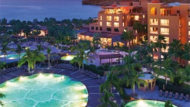 Ein Resort mit Pool, Palmen und Blick auf das Meer bei Sonnenuntergang.