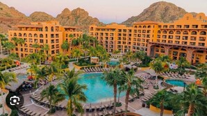 Ein Hotel mit mehreren Gebäuden, einem zentral gelegenen Schwimmbad und Palmen.