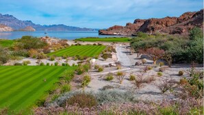 Ein Golfplatz mit Blick auf einen See und Berge im Hintergrund.