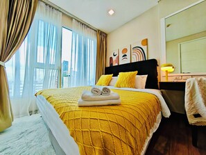 Ein Hotelzimmer mit einem großen Bett, Blick auf die Stadt, einem Schreibtisch mit Lampe und Kunstwerken an der Wand.