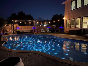 A swimming pool with illuminated patterns, outdoor furniture, and a wooden deck.