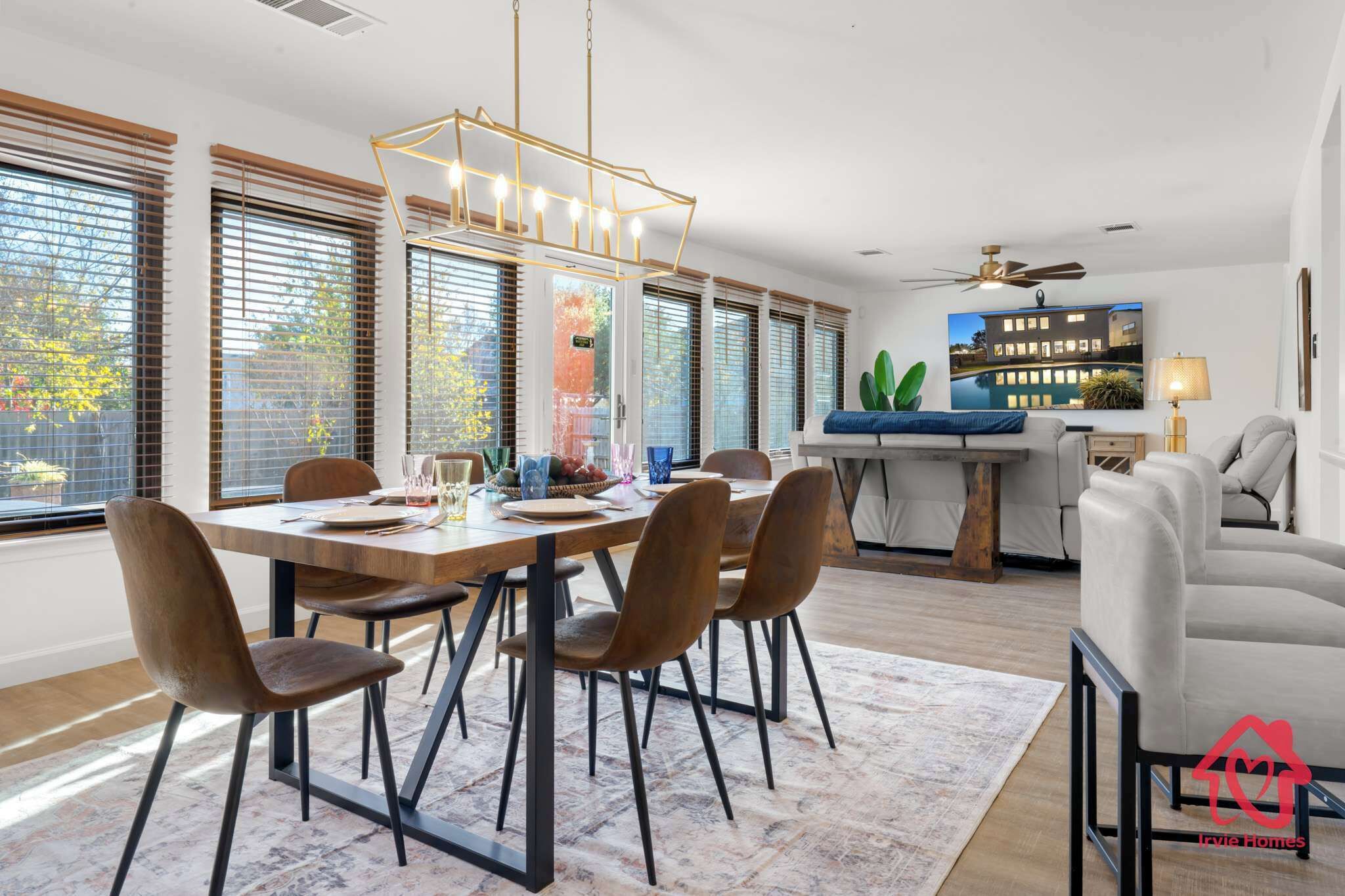 Un espace repas moderne avec une table en bois, des chaises marron et un lustre. On y trouve également un coin cuisine avec un plan de travail bleu et un ventilateur de plafond.