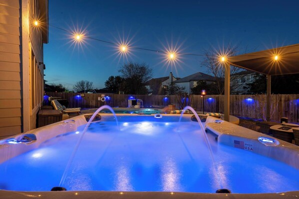 A hot tub with a blue light, surrounded by a wooden fence and a covered patio area.