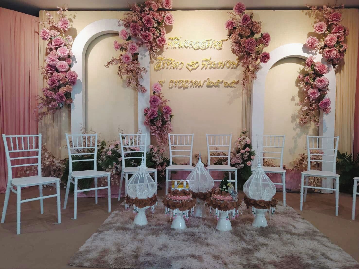 A stage with floral decorations, white chairs, and a furry rug.