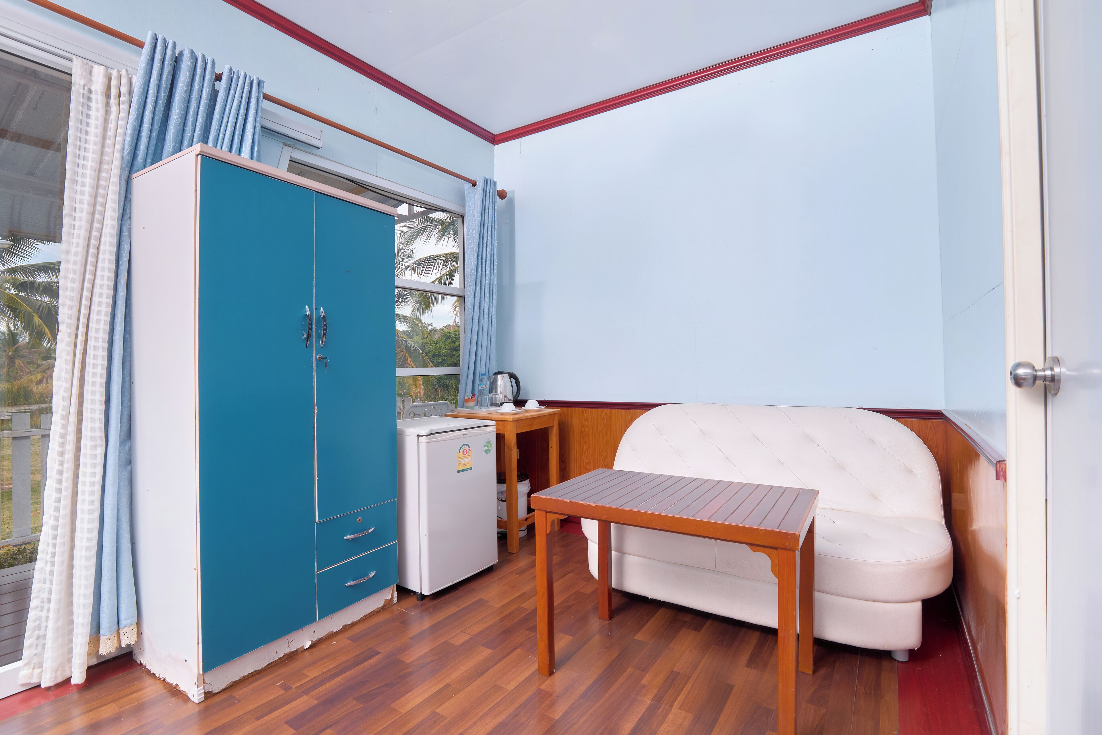 Una habitación con un armario azul, un sofá blanco, una mesa de madera y una pequeña cocina americana.