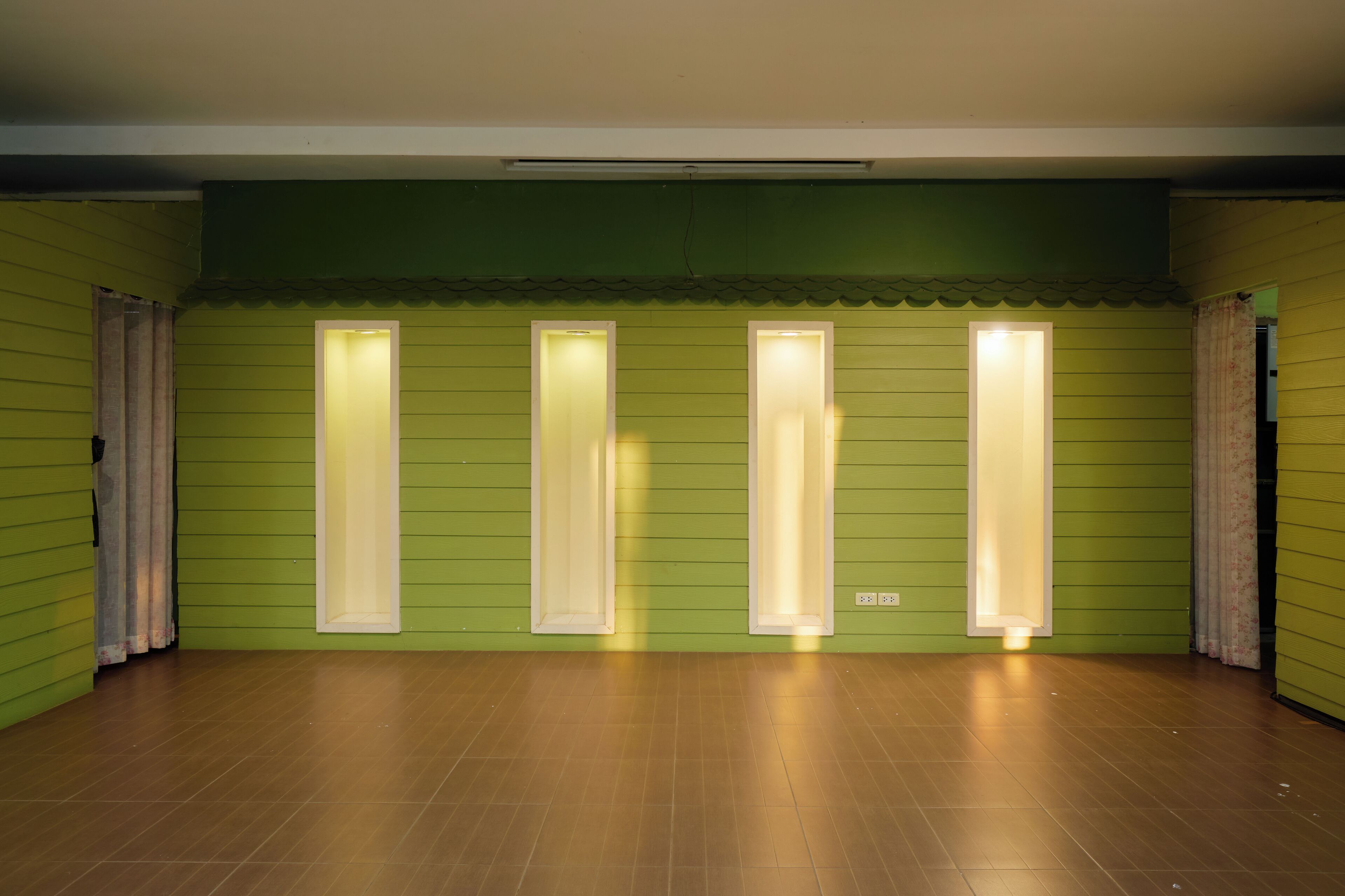 A room with green walls, four illuminated windows, and a wooden floor.